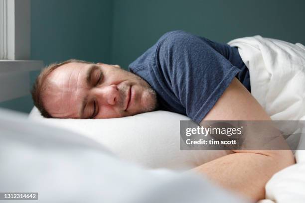 man sleeping in bed, smiling, side view - bed on white background stock-fotos und bilder