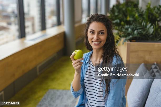 businesswoman having healthy snack, eating apple at work - adult female eating an apple stock pictures, royalty-free photos & images