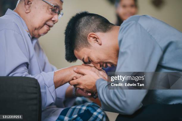 malay muslim grandson in traditional costume showing apologize gesture to his grandfather during aidilfitri celebration  malay family at home celebrating hari raya - ramadan greeting stock pictures, royalty-free photos & images