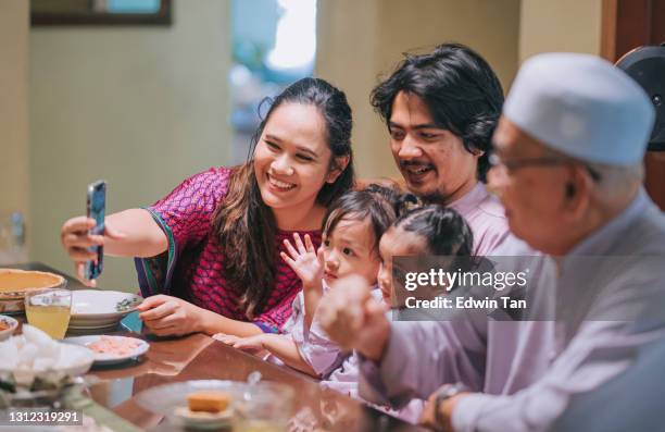 iftar ramadan hari raya malaysian muslim multi generation family waving videocall relative enjoying dinner at home in dining room - ramadhan stock pictures, royalty-free photos & images