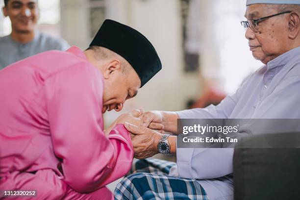 malay muslim son in traditional costume showing apologize gesture to his father during aidilfitri celebration  malay family at home celebrating hari raya - ramadan greeting stock pictures, royalty-free photos & images