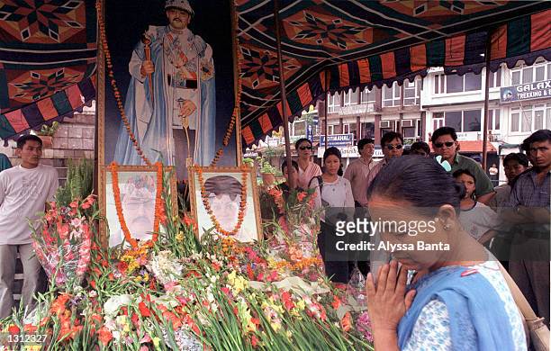 Woman prays as she passes flowers offered at a shrine with a portrait of Nepalese King Birendra and a photograph of the King and Queen Aishworya,...