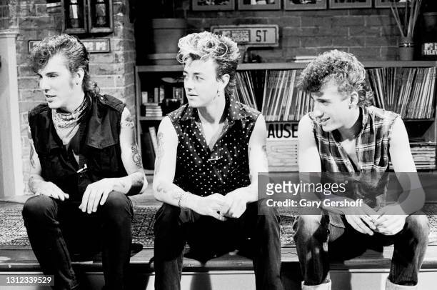 View of, from left, Rockabilly musicians 'Slim' Jim Phantom , Brian Setzer, and Lee Rocker , all of the band the Stray Cats, as they sit on a low...