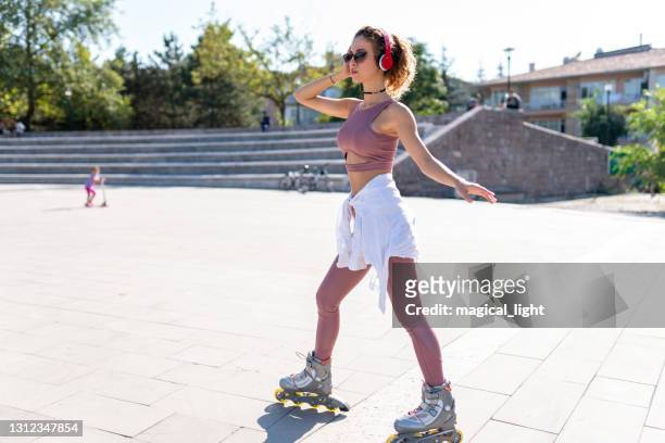 young fit woman on roller skates riding outdoors on urban streeton sunny day - roller skating in park stock pictures, royalty-free photos & images