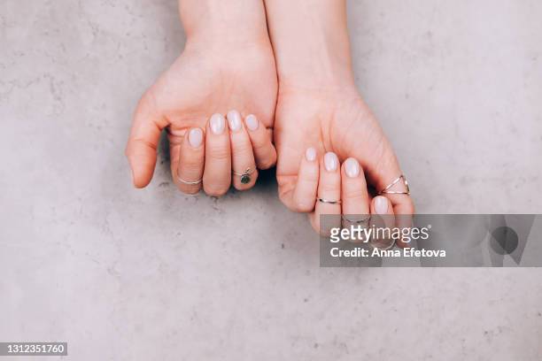 woman hands with nude pink manicure and with many various silver rings on fingers on concrete gray background. concept of trendy boho style. flat lay style with copy space - hudfärgad bildbanksfoton och bilder