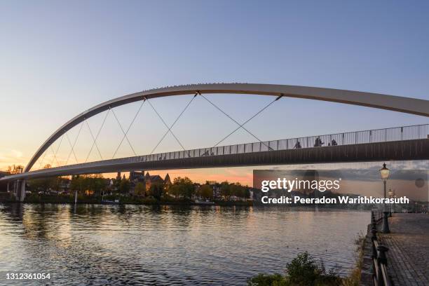 outdoor scenery on riverside of meuse river and hoge brug, modern pedestrian bridge, during sunset time and dramatic twilight sky in maastricht, netherlands. - meuse river stockfoto's en -beelden