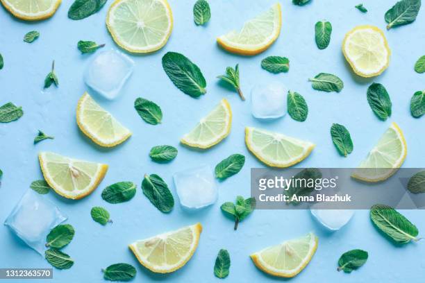 summer background. slices of lemon, mint leaves and ice cubes over blue background. - icecubes stock-fotos und bilder