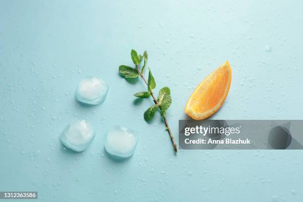 summer drink. slice of orange, branch of mint leaves and ice cubes over blue background. - mint leaves stock pictures, royalty-free photos & images