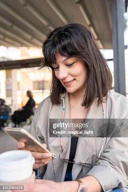 woman using smartphone with young beautiful woman holding coffee paper. - senf stock pictures, royalty-free photos & images