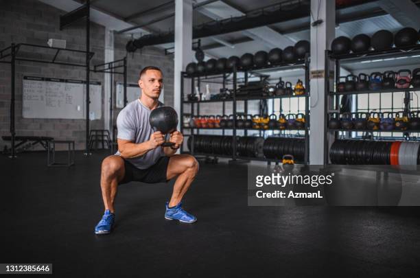 atleta masculino caucásico haciendo kettlebell sumo en cuclillas en el gimnasio - hombre agachado fotografías e imágenes de stock