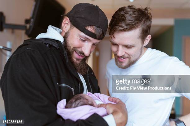 zwei männer halten neugeborenes baby zusammen im krankenhaus - family photo in the delivery room stock-fotos und bilder