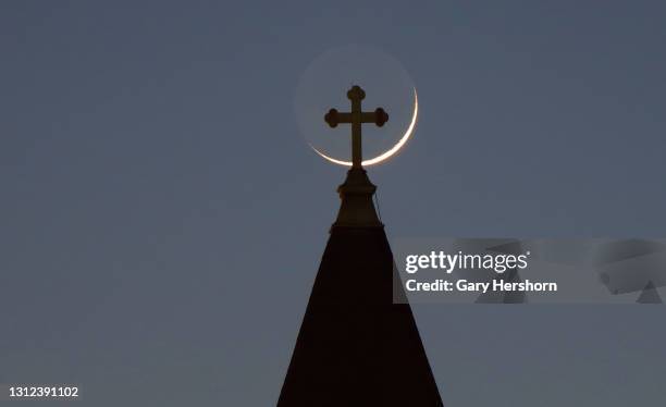 Three percent waxing crescent moon sets behind the cross on top of St. Lucy's Church on April 13, 2021 in Jersey City, New Jersey.