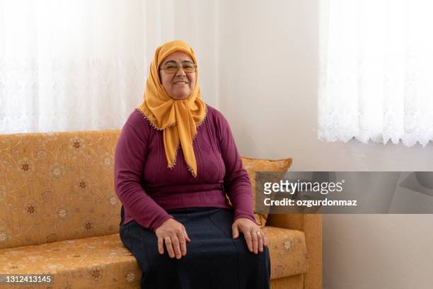 porträt einer seniorin, die auf einem sofa im wohnzimmer sitzt, mugla türkei - eine seniorin allein stock-fotos und bilder