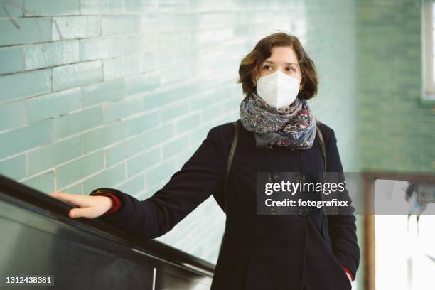 junge frau mit ffp2-maske auf einer rolltreppe - pollution mask stock-fotos und bilder