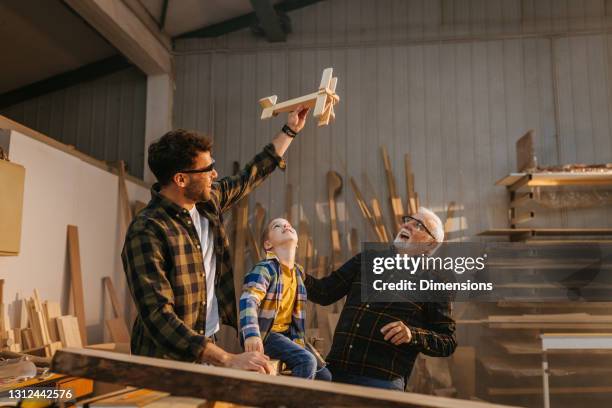 family of carpenters playing with wooden toy in workshop - grandpa son stock pictures, royalty-free photos & images