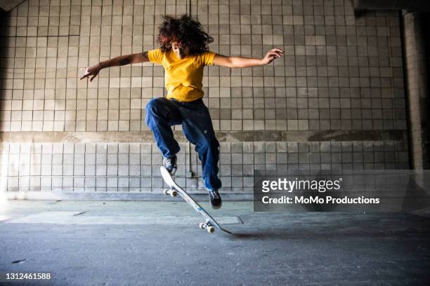 female skateboarder performing jump in warehouse environment - skating stock pictures, royalty-free photos & images