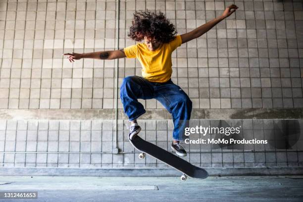 female skateboarder performing jump in warehouse environment - skateboard foto e immagini stock