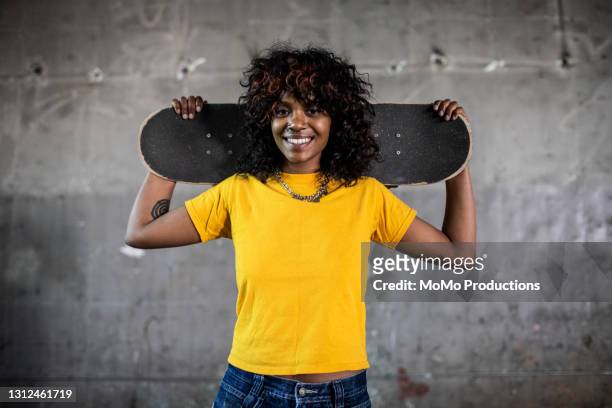 portrait of female skateboarder in warehouse environment - tee stock pictures, royalty-free photos & images