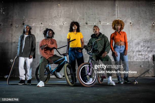 portrait of bmx riders and skateboarders in warehouse environment - black woman riding bike foto e immagini stock