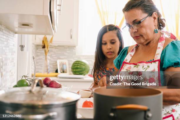 grandmother teaching granddaughter to cook in kitchen at home - tradición fotografías e imágenes de stock