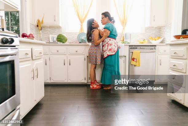 grandmother kissing grandchild in kitchen at home - hispanic grandmother stock pictures, royalty-free photos & images
