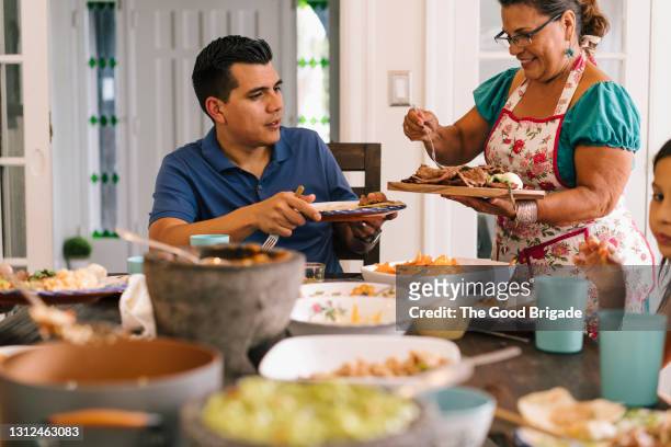 grandmother serving food to family at dinner table - à profusion - fotografias e filmes do acervo