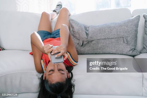 young girl lying on sofa looking at smartphone - day 11 fotografías e imágenes de stock