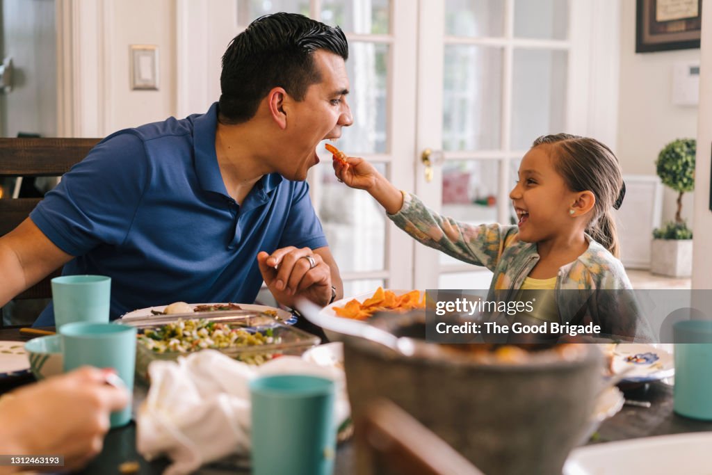 Young girl feeding her father at dinner table