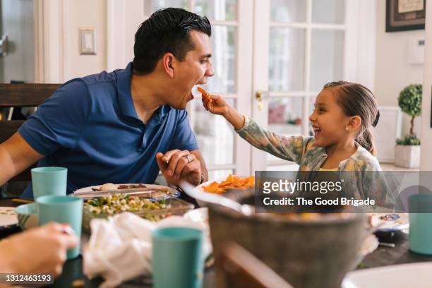 young girl feeding her father at dinner table - happy family eating photos et images de collection