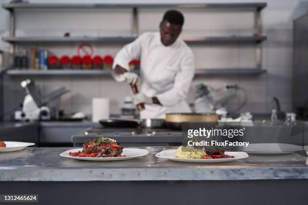 jamaican chef using a salt and pepper shaker to season the beef steak - jamaican ethnicity imagens e fotografias de stock