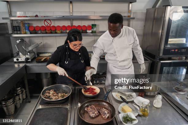 chef-kok die de consistentie van een granaatappelsaus controleert, zijn vrouwelijke voorbereide medewerker - avondschool stockfoto's en -beelden