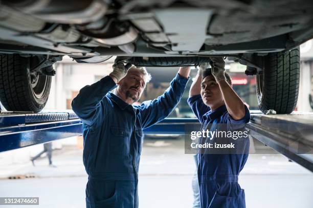 mature car mechanic and apprentice at work - mechanic uniform stock pictures, royalty-free photos & images