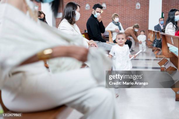 baby 1 to 2 years old walks through the church during her christening ceremony while wearing her dress for the occasion and holding her christening candle in hand. - vicar stock pictures, royalty-free photos & images