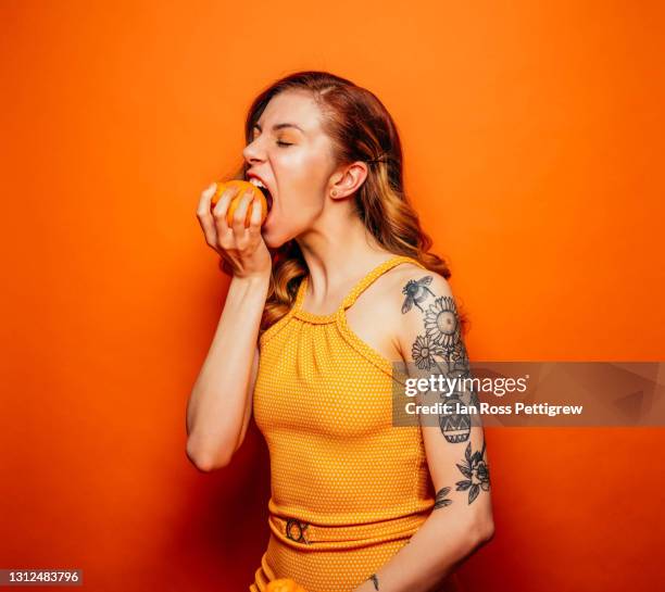 beautiful young woman biting into an orange - orange fruit stock-fotos und bilder