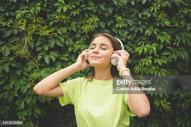 young caucasian brunette girl with headphones outdoors on sunny summer day. - mp3 player stock pictures, royalty-free photos & images