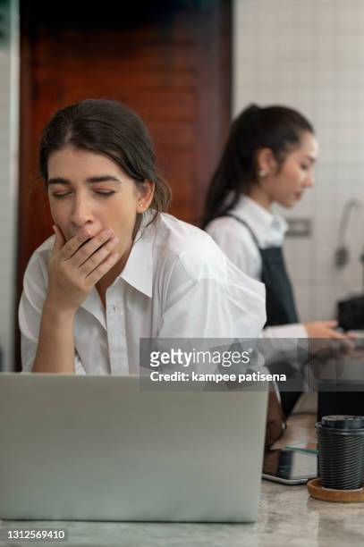 young female tired caucasian barista yawning at work place in cafe. - yawn office stockfoto's en -beelden