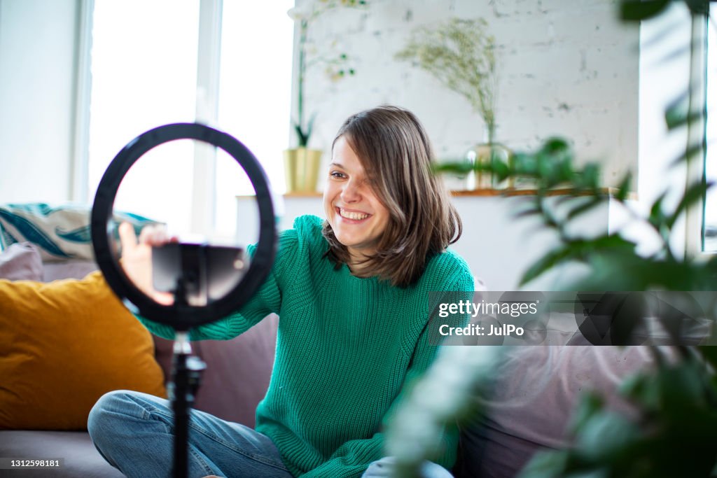 Young influencer woman streaming live video with smartphone and led