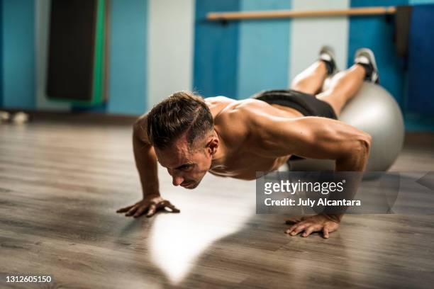 man in gym trains push-ups on the floor helping himself with a sports ball - pectoral muscle stock pictures, royalty-free photos & images