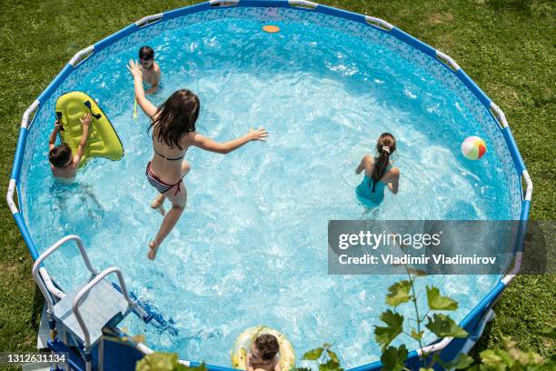 a high view of a girl leaping into a sparkling swimming pool while her siblings stay out of her way - swimming pool stock pictures, royalty-free photos & images