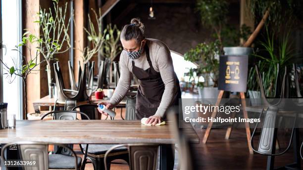 waiter disinfecting tables in restaurant, coronavirus and new normal concept. - restaurants open during lockdown stock pictures, royalty-free photos & images