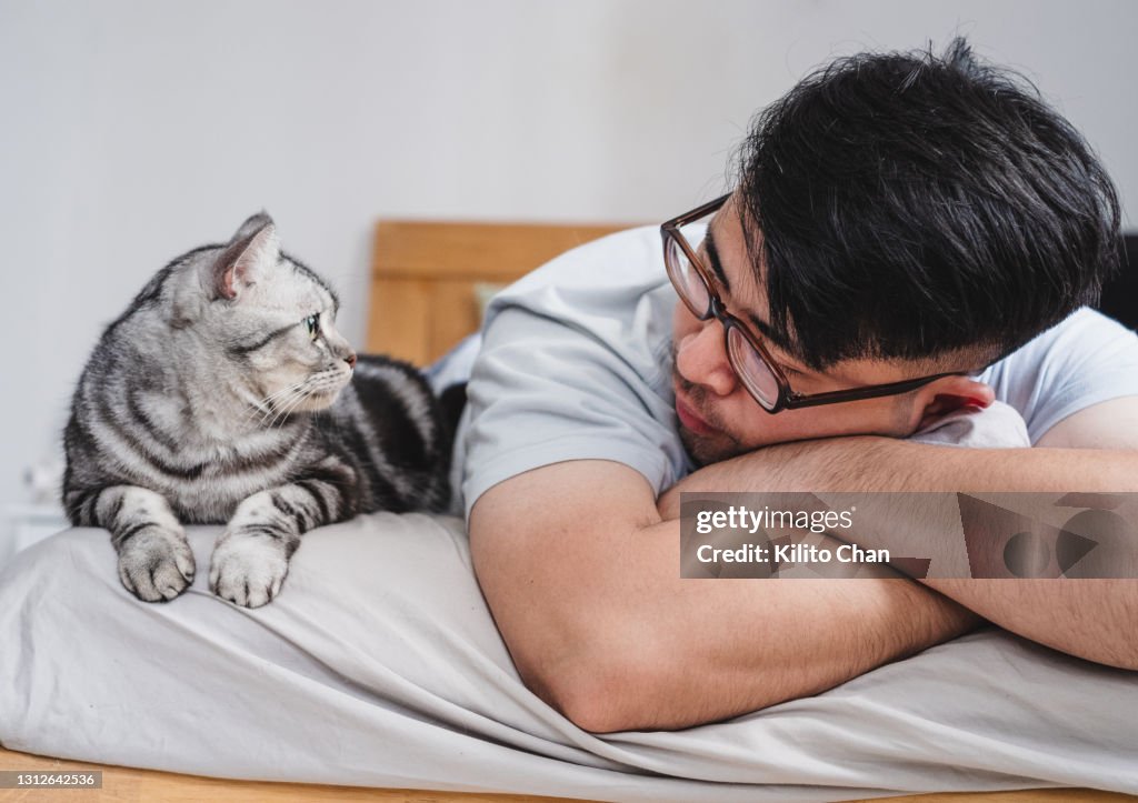 Asian man lying on bed with his cat and looking at each other