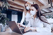 Two female colleagues working in office together wearing medical masks