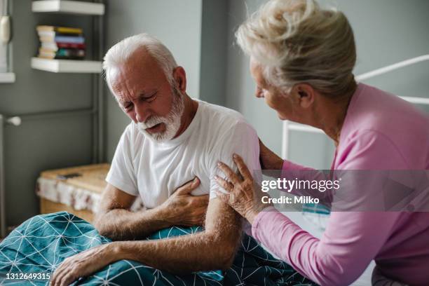 senior mann leidet unter brustschmerzen im bett - breathing chest stock-fotos und bilder