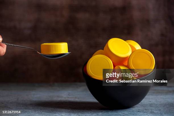 bowl with yellow plastic lids, with human hand and metal spoon, plastic contamination. - food contamination stock pictures, royalty-free photos & images