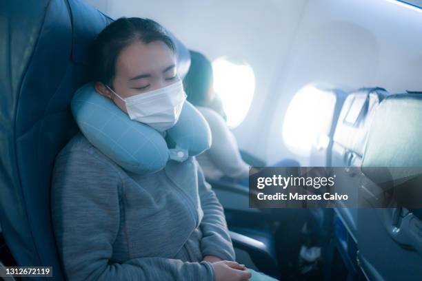 tourism and flying in times of covid19 - young sweet and tired Asian Japanese woman in face mask sitting on airplane cabin sleeping peacefully during flight