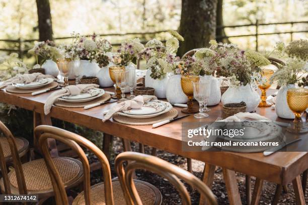 rural wedding reception in the forest with wooden table and colored glasses and floral decoration - table decoration stockfoto's en -beelden