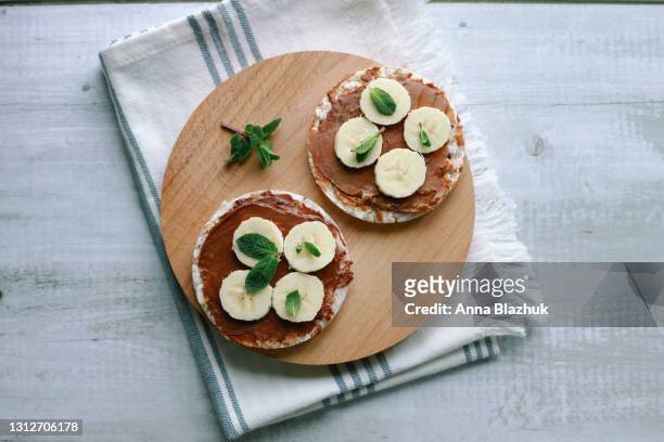 healthy vegan snack or breakfast meal made of puffed rice cakes, peanut chocolate butter, banana and mint - rice cakes stock pictures, royalty-free photos & images