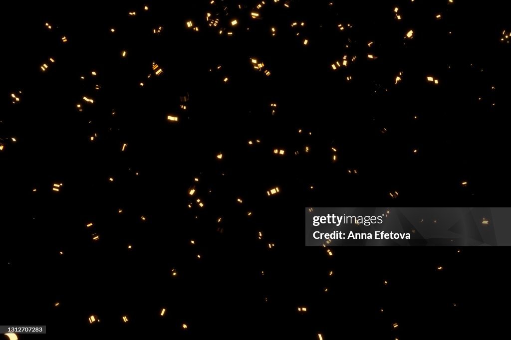 Glittering golden confetti on black isolated background. Christmas and New Year concept in trendy festive golden color.