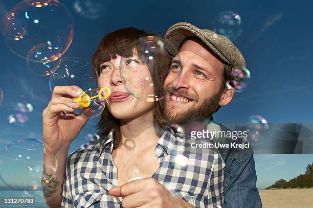 young couple blowing bubbles on beach, close up - bubbles happy stock-fotos und bilder