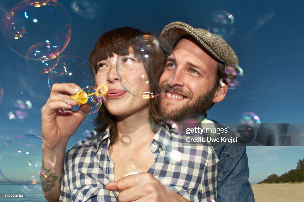 Young couple blowing bubbles on beach, close up